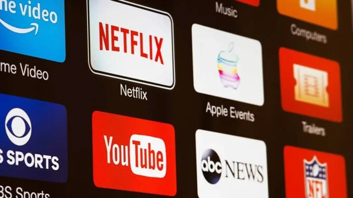 Controle remoto apontado para uma smart TV exibindo vários logos de aplicativos de streaming como Netflix, Disney+, Prime Video e Max