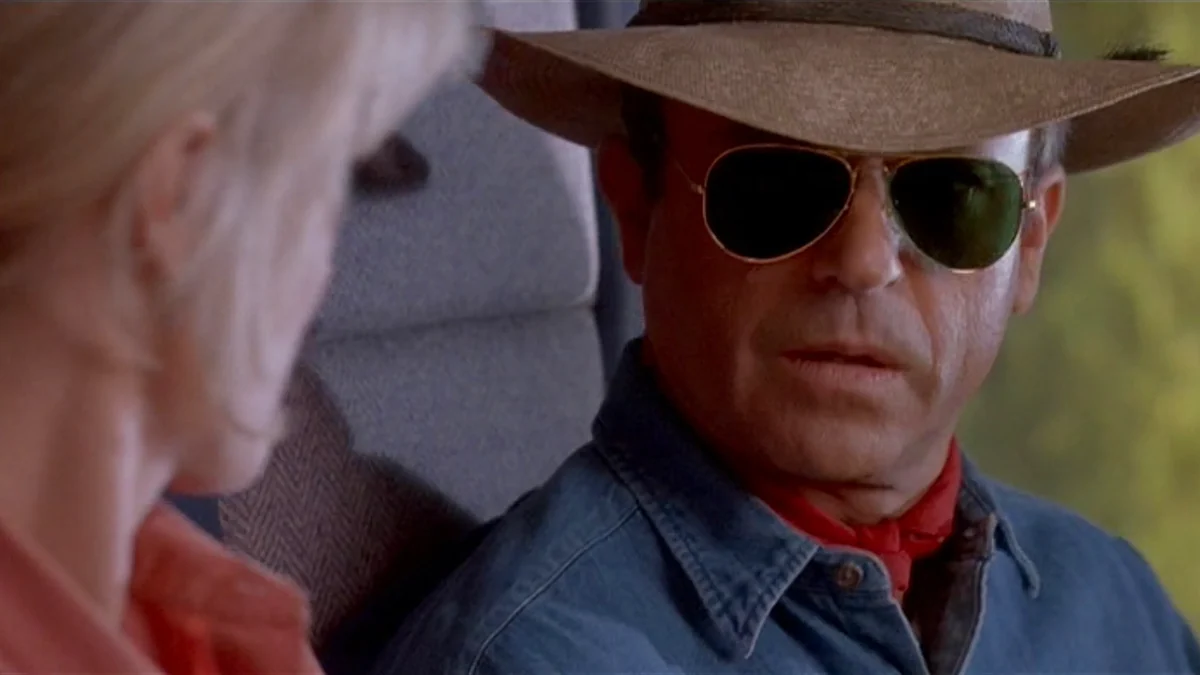 Sam Neill como o Dr. Alan Grant, ao lado da cerca elétrica, em cena de Jurassic Park (1993)