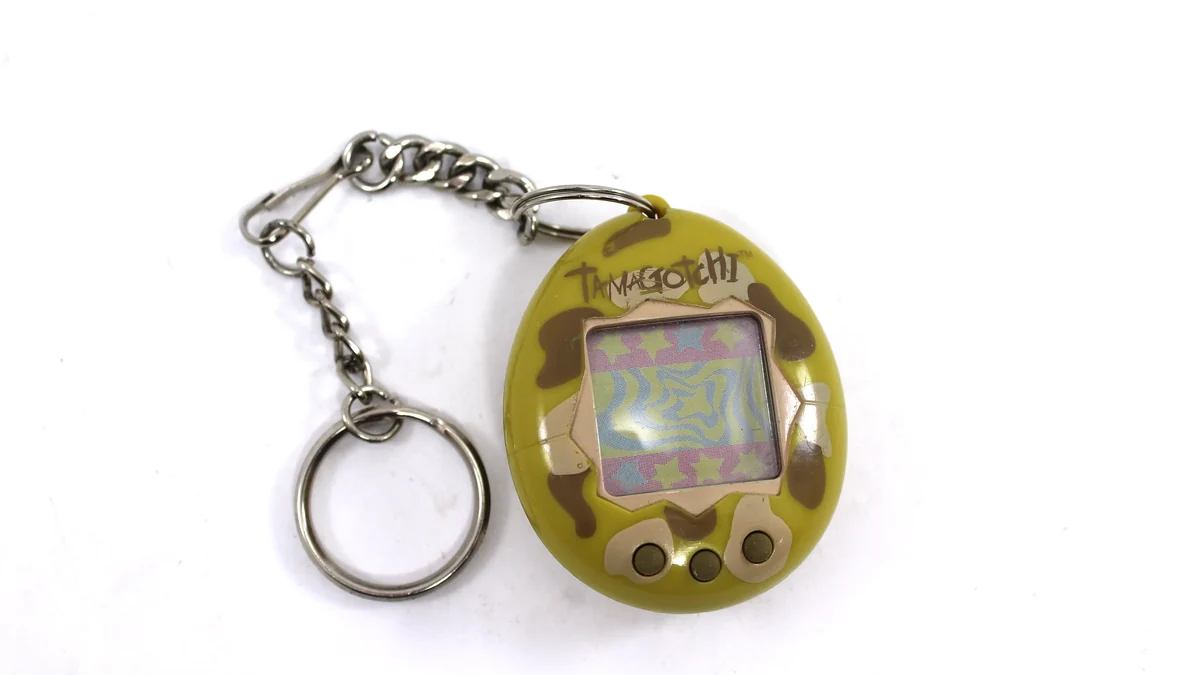Tamagotchi original de 1996 em formato de ovo com corrente de chaveiro, tela monocromática pixelada mostrando um bichinho virtual